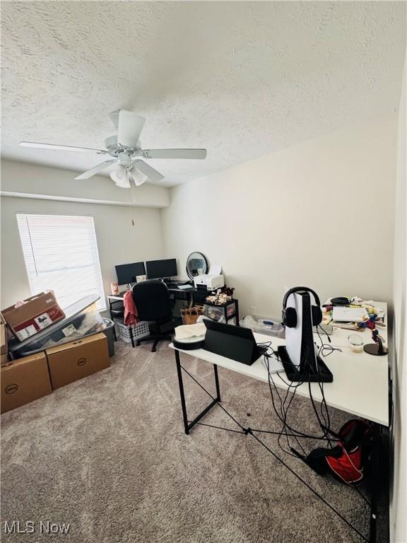 carpeted home office with a textured ceiling and ceiling fan