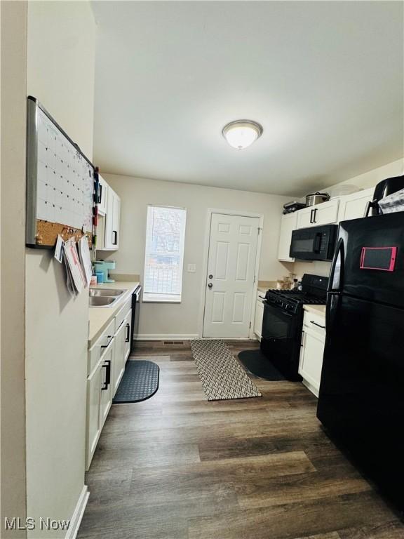 kitchen with white cabinetry, dark wood-type flooring, black appliances, and sink