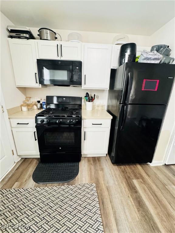 kitchen with light hardwood / wood-style flooring, white cabinetry, and black appliances