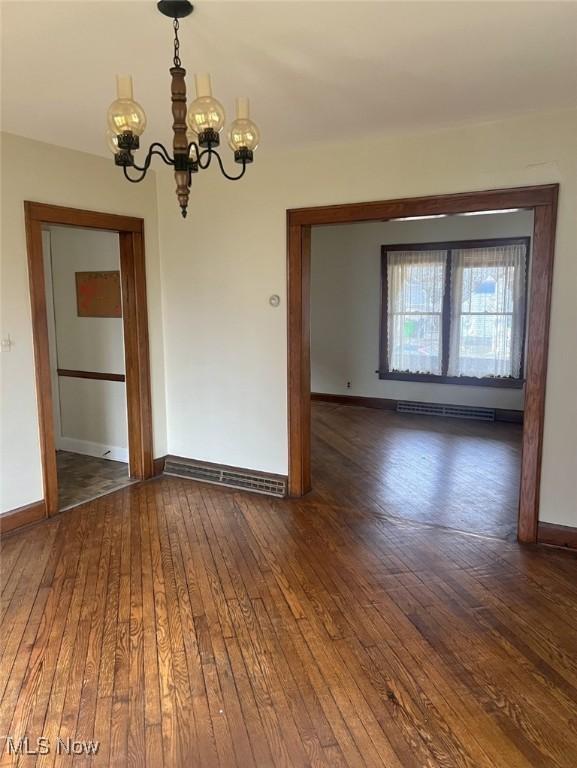 empty room featuring a notable chandelier, dark hardwood / wood-style floors, and a baseboard heating unit