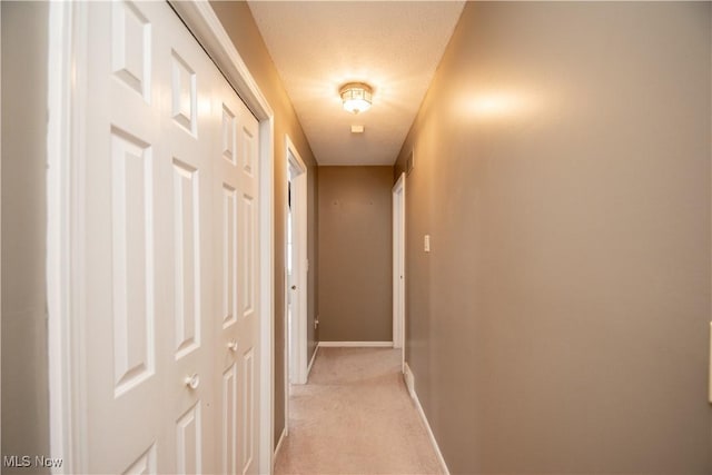 corridor with light colored carpet, baseboards, and a textured ceiling