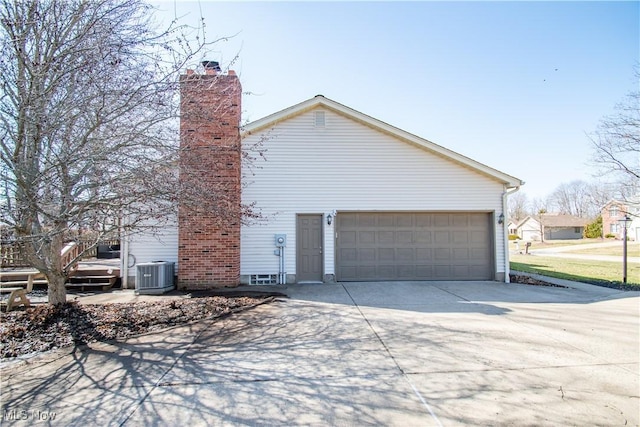 view of side of home with an attached garage, central AC unit, concrete driveway, and a chimney