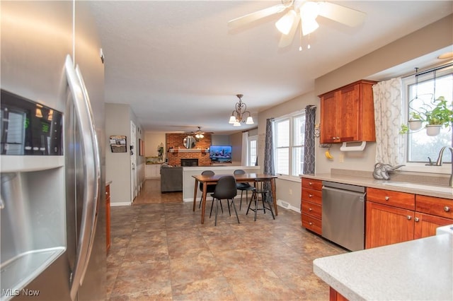 kitchen with brown cabinetry, a sink, appliances with stainless steel finishes, ceiling fan with notable chandelier, and open floor plan