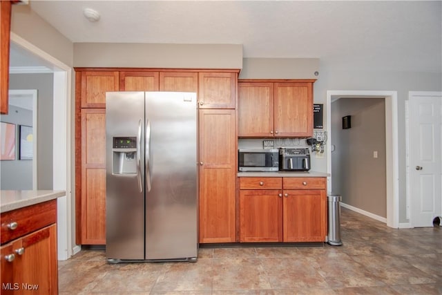 kitchen with brown cabinetry, baseboards, stainless steel appliances, light countertops, and backsplash