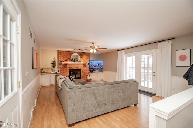 living room featuring visible vents, a wainscoted wall, a fireplace, light wood-style floors, and a ceiling fan