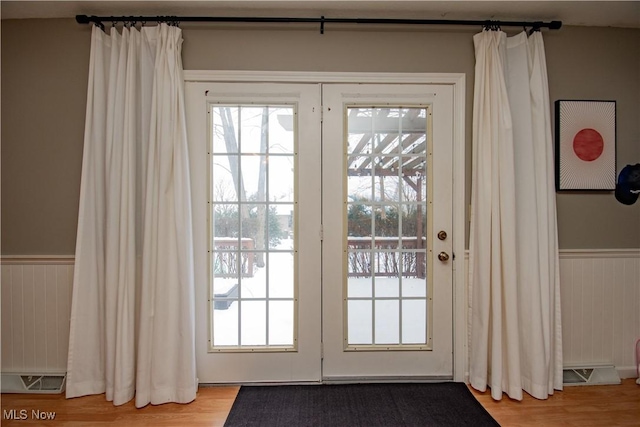 doorway to outside with wood finished floors and wainscoting