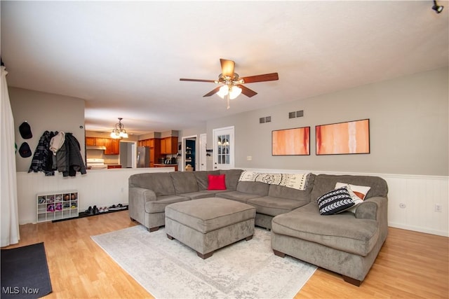 living area featuring light wood-type flooring, visible vents, wainscoting, and ceiling fan with notable chandelier