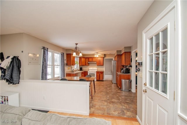 kitchen with white range with electric cooktop, freestanding refrigerator, under cabinet range hood, brown cabinets, and a chandelier