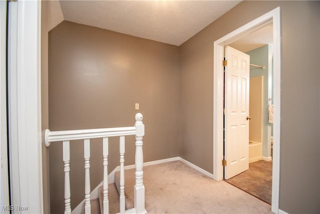 corridor featuring an upstairs landing, lofted ceiling, a textured ceiling, carpet, and baseboards