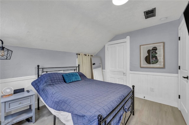 bedroom with a textured ceiling, light hardwood / wood-style flooring, and vaulted ceiling