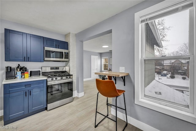 kitchen featuring blue cabinetry, a kitchen breakfast bar, light wood-type flooring, and stainless steel appliances