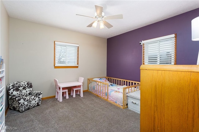 carpeted bedroom with ceiling fan and a nursery area