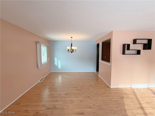 spare room featuring a chandelier and light wood-type flooring