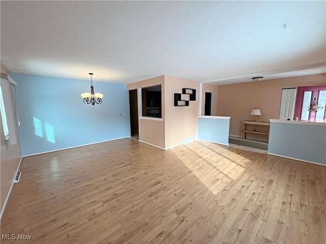 unfurnished living room with light wood-type flooring and an inviting chandelier