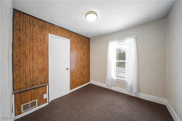 unfurnished bedroom featuring wood walls and dark carpet