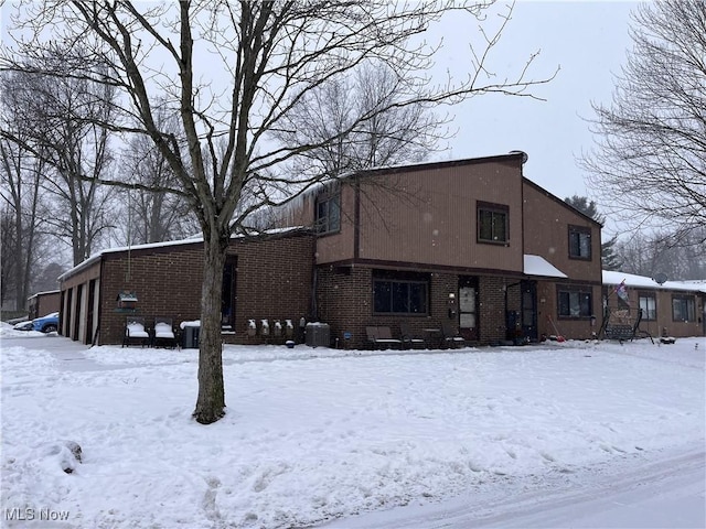 snow covered rear of property featuring central AC unit