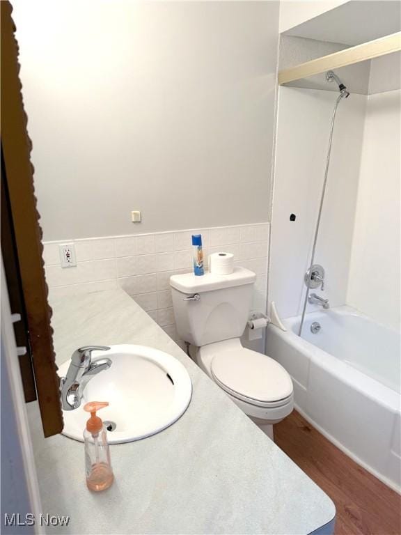 full bathroom with toilet, tile walls, wood-type flooring, sink, and shower / bath combination