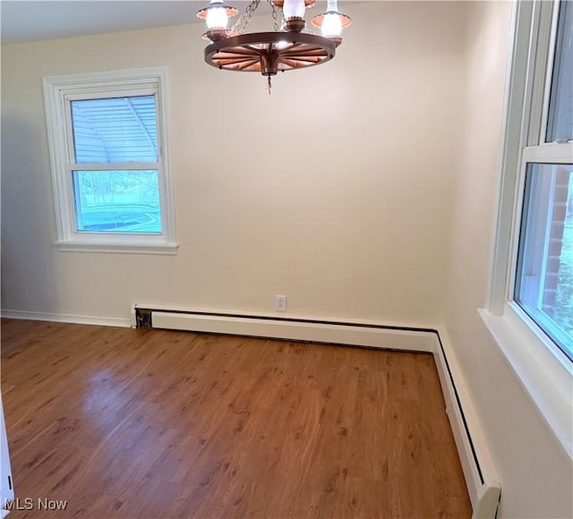 unfurnished dining area with a baseboard heating unit, a chandelier, and hardwood / wood-style floors