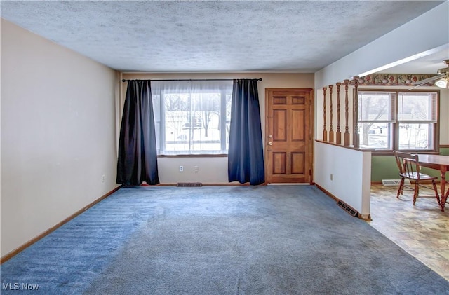 carpeted spare room featuring a textured ceiling, ceiling fan, and a healthy amount of sunlight