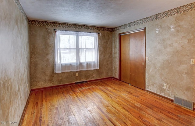 unfurnished bedroom featuring a closet, light hardwood / wood-style floors, and a textured ceiling