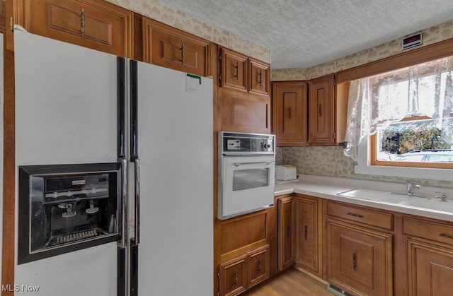 kitchen with a textured ceiling, sink, light hardwood / wood-style floors, and white appliances