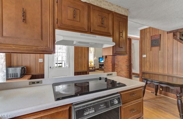 kitchen featuring black appliances, wooden walls, a textured ceiling, light hardwood / wood-style floors, and brick wall