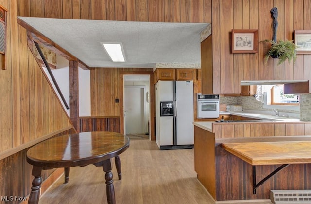 kitchen featuring kitchen peninsula, wood walls, light hardwood / wood-style flooring, and white appliances