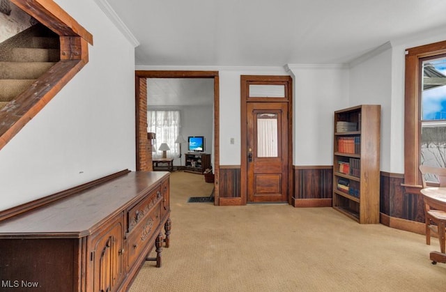 carpeted foyer with ornamental molding and wood walls