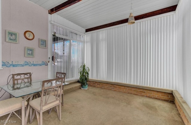 carpeted dining area with beamed ceiling