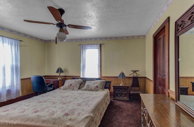 carpeted bedroom with ceiling fan, wooden walls, and a textured ceiling