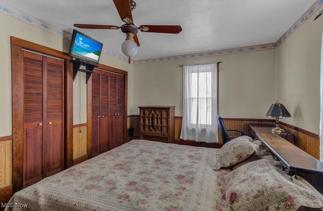 bedroom featuring two closets, ceiling fan, and wooden walls