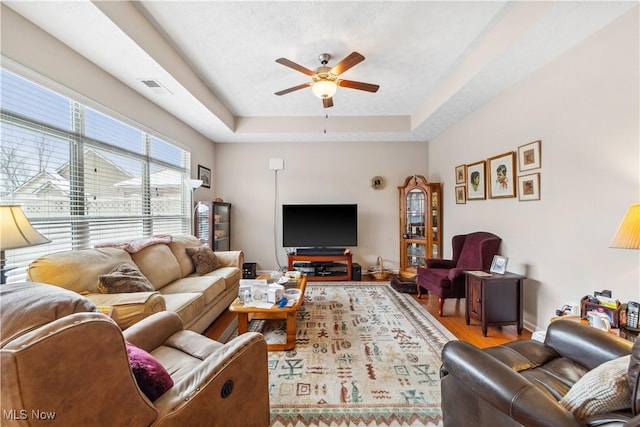 living room featuring ceiling fan, a tray ceiling, and light hardwood / wood-style flooring