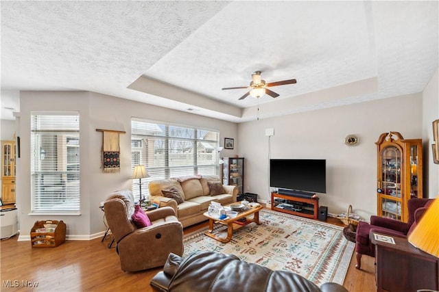 living room featuring a raised ceiling, ceiling fan, light hardwood / wood-style floors, and a textured ceiling