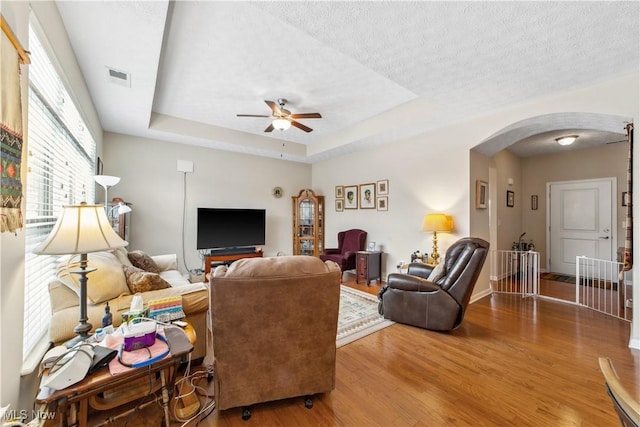 living room featuring a raised ceiling, ceiling fan, a textured ceiling, and hardwood / wood-style floors