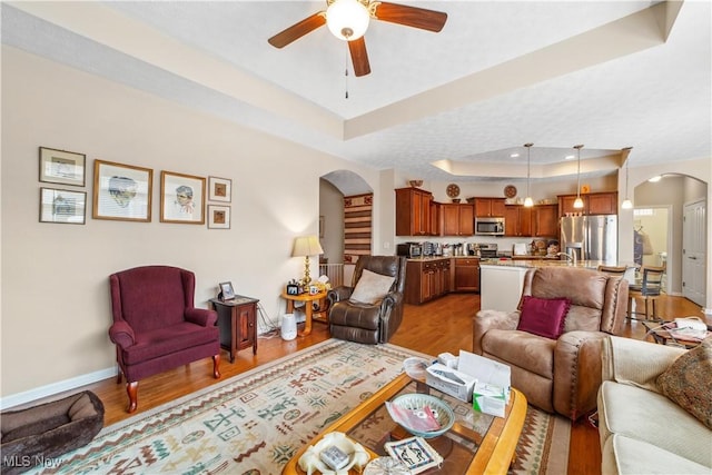 living room featuring hardwood / wood-style flooring, a raised ceiling, and ceiling fan