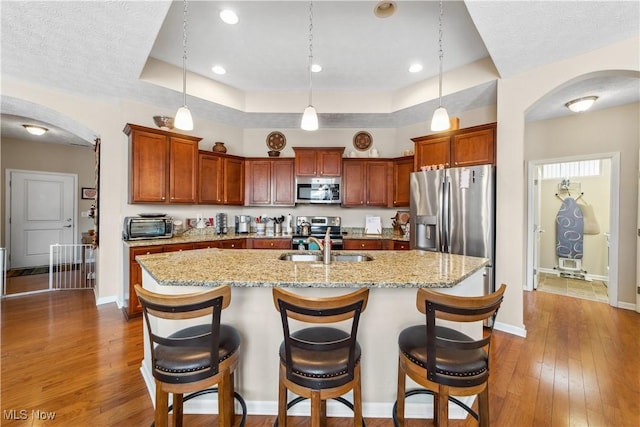 kitchen with stainless steel appliances, a breakfast bar area, a kitchen island with sink, and pendant lighting