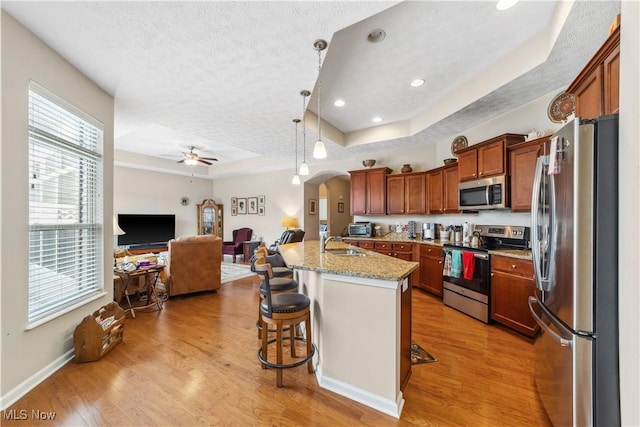 kitchen featuring a kitchen breakfast bar, a center island with sink, appliances with stainless steel finishes, light stone counters, and a tray ceiling