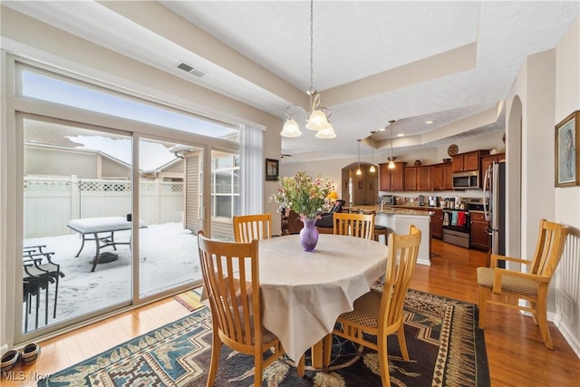 dining space with hardwood / wood-style flooring, a raised ceiling, a textured ceiling, and a chandelier