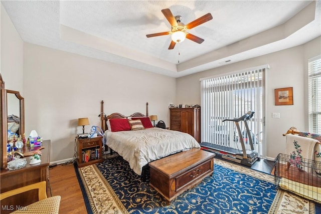 bedroom with a raised ceiling, ceiling fan, wood-type flooring, and multiple windows