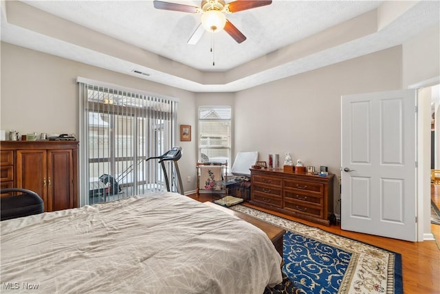 bedroom featuring a raised ceiling, ceiling fan, and light wood-type flooring