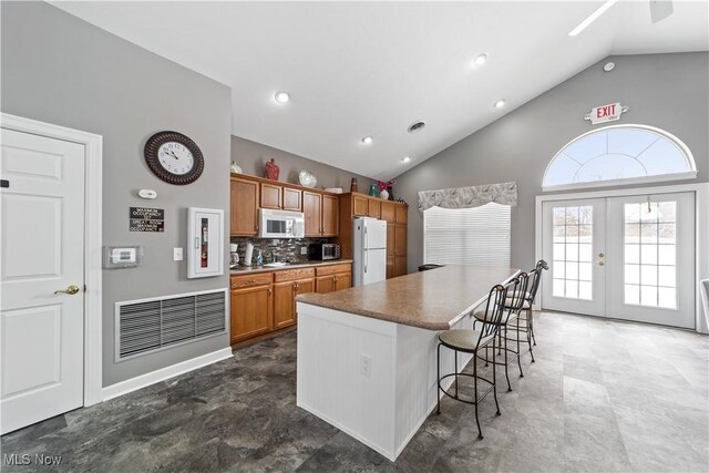 kitchen featuring white appliances, french doors, high vaulted ceiling, backsplash, and a breakfast bar area