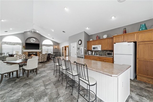 kitchen featuring white appliances, vaulted ceiling, a breakfast bar area, ceiling fan, and tasteful backsplash