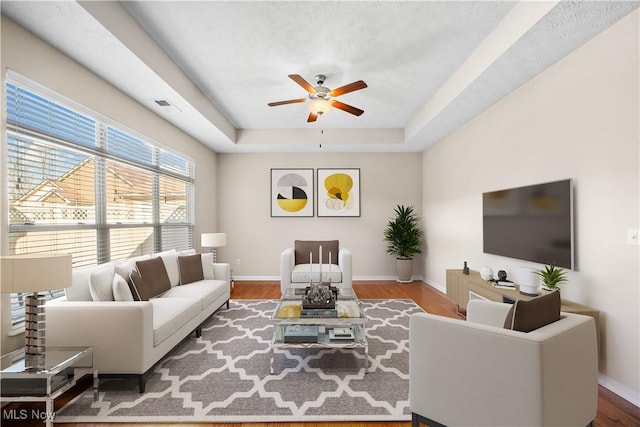 living room with wood-type flooring, a raised ceiling, and ceiling fan