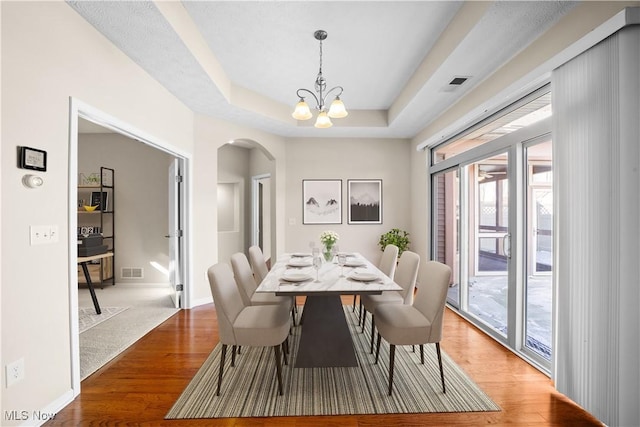 dining room featuring an inviting chandelier, a tray ceiling, and light hardwood / wood-style floors