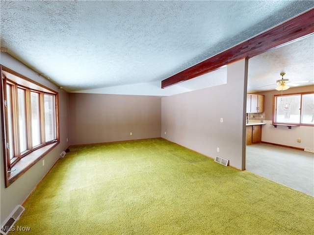 carpeted empty room featuring a textured ceiling, lofted ceiling with beams, and ceiling fan