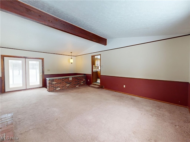 carpeted spare room with a brick fireplace, a textured ceiling, and vaulted ceiling with beams