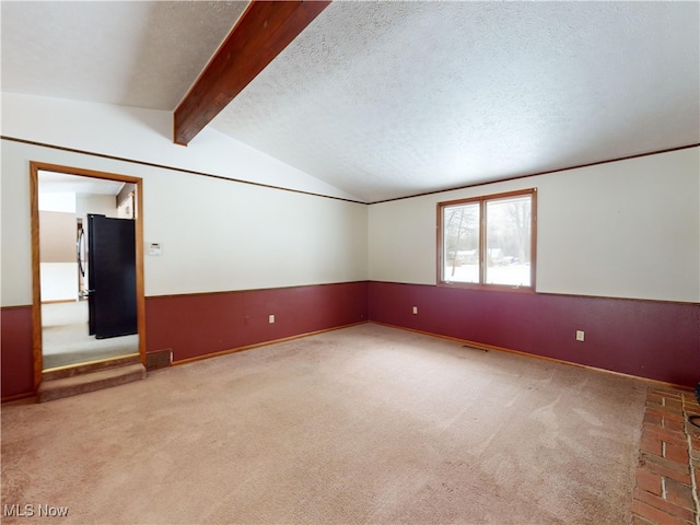 carpeted spare room with a textured ceiling and vaulted ceiling with beams