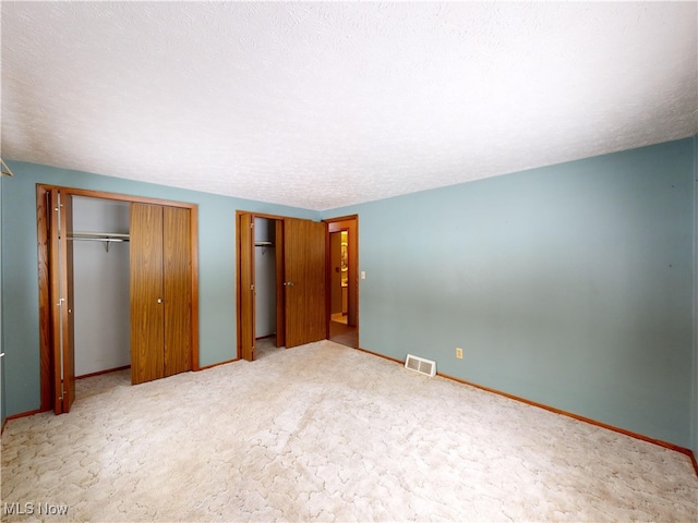 unfurnished bedroom with a textured ceiling, two closets, and carpet flooring