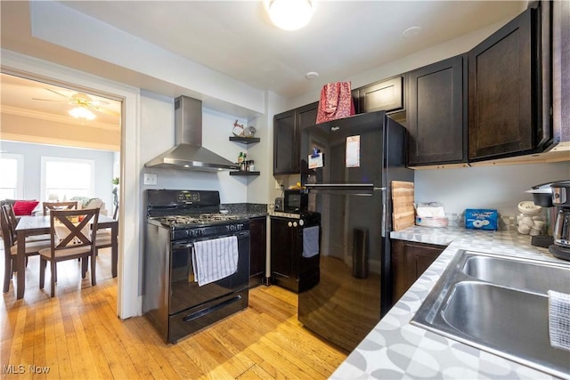 kitchen featuring sink, wall chimney exhaust hood, light wood-type flooring, dark brown cabinets, and black appliances