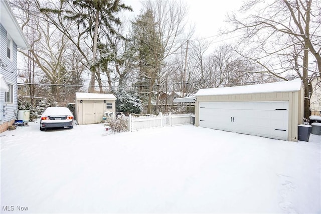 yard layered in snow featuring a garage and a storage unit